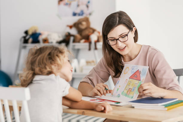 istockphoto-1011888356-612×612 A professional child education therapist having a meeting with a kid in a family support center.